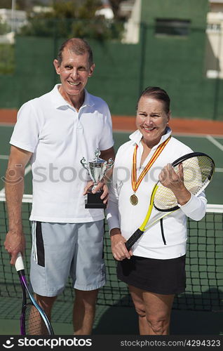 Older couple with trophy on tennis court