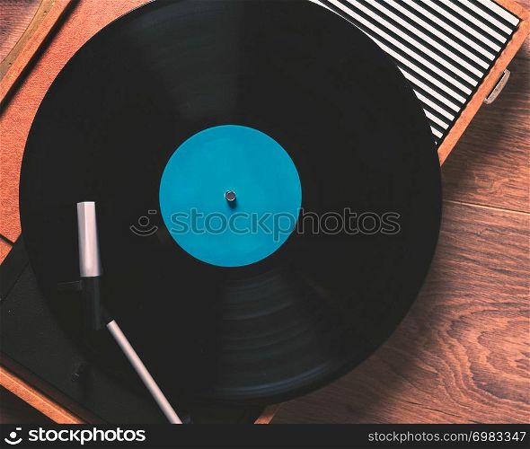 Older Gramophone with a vinyl record on wooden table, top view close up,vintage style.