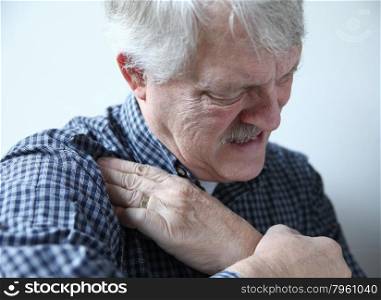 older man grimaces and touches area of pain in his shoulder