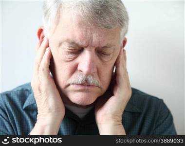 Older man holds both hands to his upper jaw near the ears.