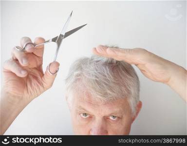 Older man holds scissors and some hair, ready to cut.