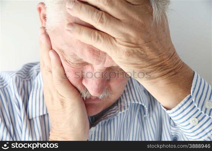 Older man in pain holds his head with both hands.