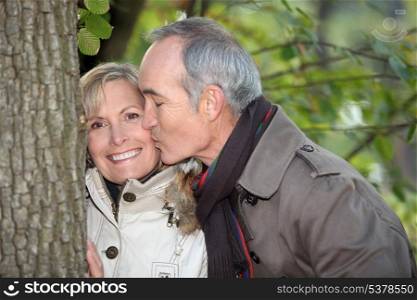 Older man kissing his partner under a tree