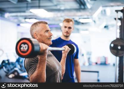 Older man lifting weights, supervised by gym assistant. Sporty lifestyle of elderly people.. Older man lifting weights, supervised by gym assistant.