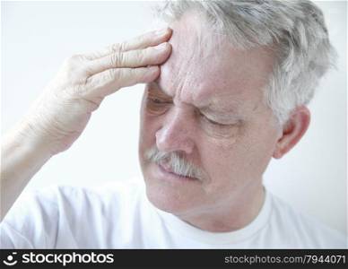 Older man puts his fingers against his forehead while frowning in pain.