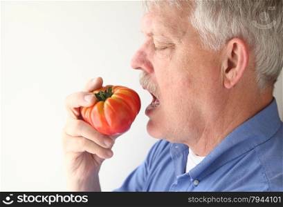 older man ready to bite into an heirloom tomato