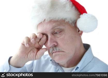 older man rubs his eye while wearing Santa hat