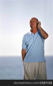 Older man taking a call by the sea