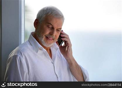 Older man with a phone by a window