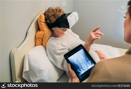 Older patient using virtual reality glasses to see her spine while female doctor explains. Older patient using virtual reality glasses