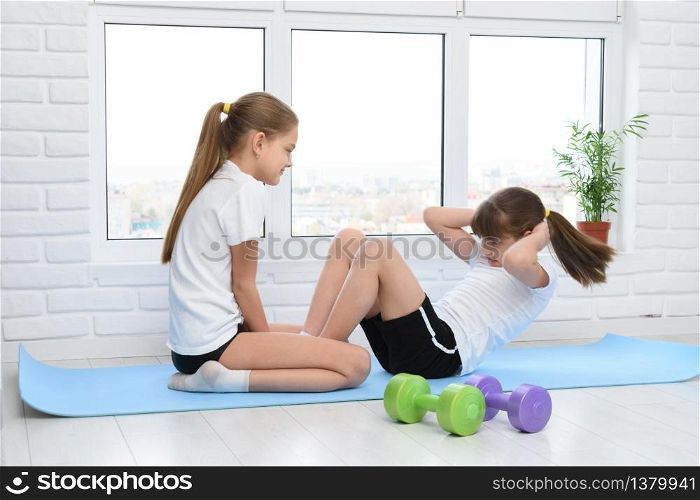 Older sister helps younger to do exercise for the press