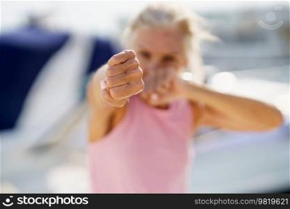 Older woman doing sport in a coastal port. Arm training throwing boxing punches. Mature Female doing shadow boxing outdoors.. Older woman doing shadow boxing outdoors. Senior female doing sport in a coastal port