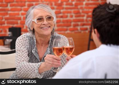 Older woman drinking rose wine in a restaurant with a young man
