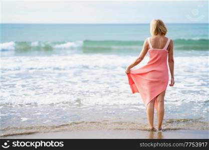 Older woman enjoying her free time looking at the sea from the shore of the beach.. Elderly female enjoying her retirement at a seaside retreat.. Older woman enjoying her free time looking at the sea from the shore of the beach.