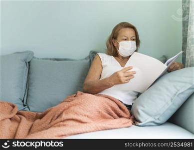 older woman with medical mask home during pandemic reading book