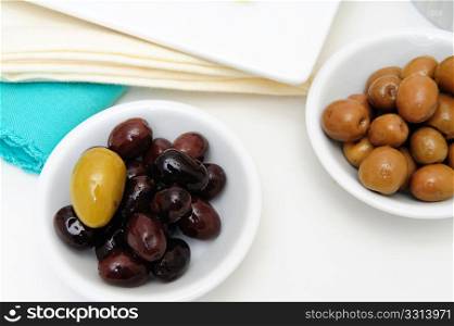 Olive Green And Black. Green and black marinated olives in small white bowls with blue and cream colored napkins in the background