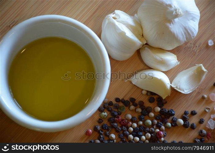 olive oil in a ramekin dish, garlic, and peppercorns on a wood cutting board
