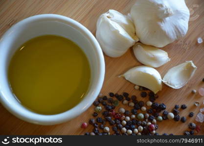 olive oil in a ramekin dish, garlic, and peppercorns on a wood cutting board