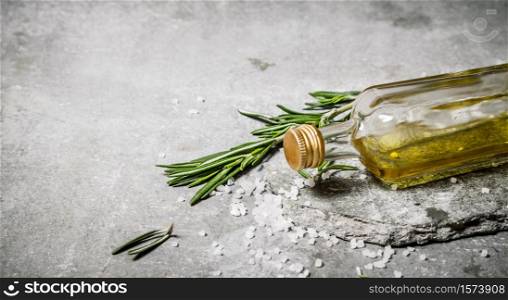 Olive oil in bottle with rosemary and salt. On a stone background.. Olive oil in bottle with rosemary and salt.