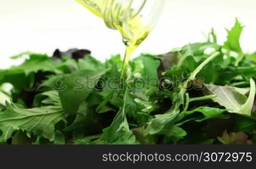 Olive oil pouring into bowl of salad