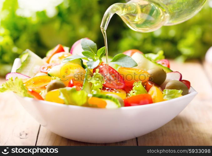 olive oil pouring into bowl of vegetable salad