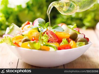 olive oil pouring into bowl of vegetable salad