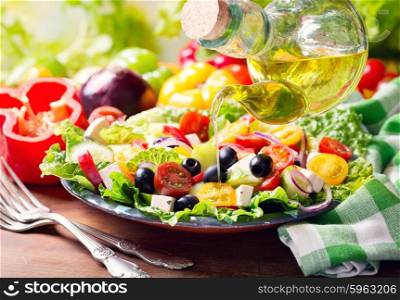 olive oil pouring into plate of fresh greek salad