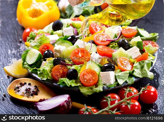 olive oil pouring into plate of salad on dark board