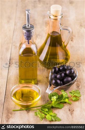 Olive oil with fresh herbs and Black olives on wooden background