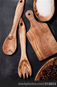 Olive wood kitchen utensils with chopping board and bowl on stone background. Top view.