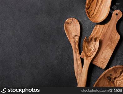 Olive wood kitchen utensils with chopping board and bowl on stone table background. Top view.