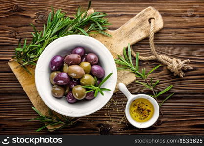 Olives in bowl with olive oil on dark wooden rustic background, above view; italian cuisine
