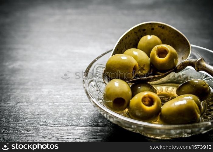Olives in olive oil with an old spoon. On black rustic background.. Olives in olive oil with an old spoon.