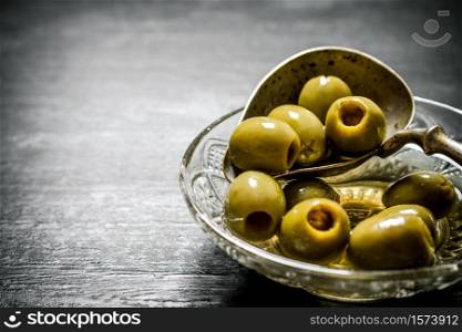 Olives in olive oil with an old spoon. On black rustic background.. Olives in olive oil with an old spoon.