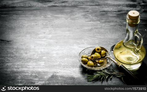 Olives with olive oil and a branch of rosemary. On black rustic background.. Olives with olive oil and a branch of rosemary.