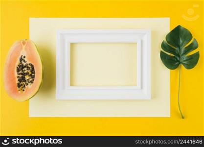 OLYMPUS DIGITAL CAMERA. halved papaya monstera leaf white wooden frame paper against yellow background