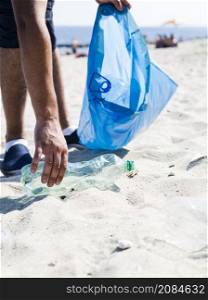 OLYMPUS DIGITAL CAMERA. man hand picking up trash plastic bottle by beach while holding blue garbage bag