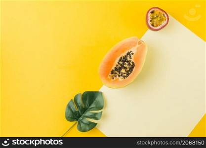 OLYMPUS DIGITAL CAMERA. overhead view artificial leaf papaya passion fruit blank paper against yellow backdrop
