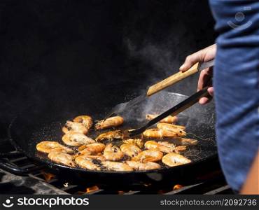 OLYMPUS DIGITAL CAMERA. unrecognizable cook flipping shrimps frying big pan