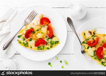 Omelet. Eggs fried. Scrambled eggs with green onion and fresh tomato. Omlette on white plate. Breakfast. Top view. White wooden background