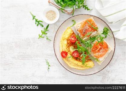 Omelette or omelet, fresh arugula and tomato salad and toasts with butter and salted salmon. Breakfast. Top view