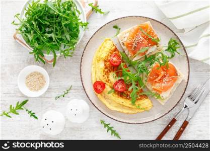 Omelette or omelet, fresh arugula and tomato salad and toasts with butter and salted salmon. Breakfast. Top view