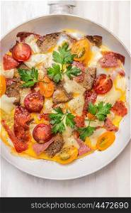 Omelette with bread, meat and tomatoes in white fry pan, top view, close up