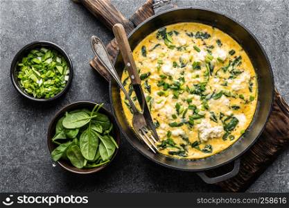 omelette with spinach and cheese in a pan on the concrete background top view
