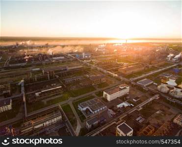 On a big site plant located distillation systems, oil reservoirs, coolers etc. A huge oil refinery with metal structures, pipes and distillation of the complex at sunset. Aerial view