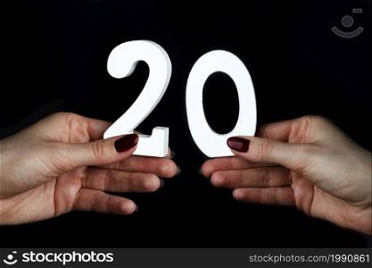 On a black background, female hand with a digit of twenty.. On the female palms figure twenty.