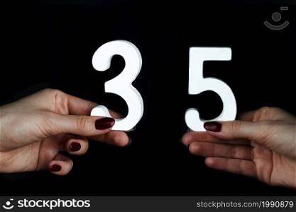 On a black background, female hand with a figure thirty-five.. On the female palms figure thirty-five.