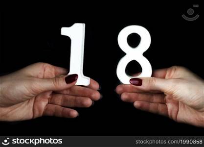 On a black background, female hand with number eighteen.. On the female palms figure eighteen.