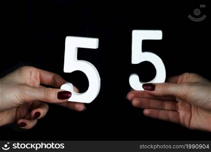 On a black background, female hand with number fifty-five.. On the female palms figure fifty-five.