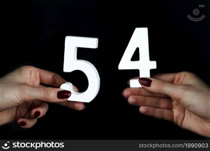On a black background, female hand with number fifty-four.. On the female palms figure fifty-four.